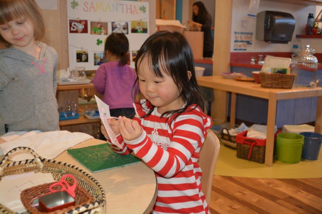 Child sitting at table working on sewing activity in Eyas Montessori classroom