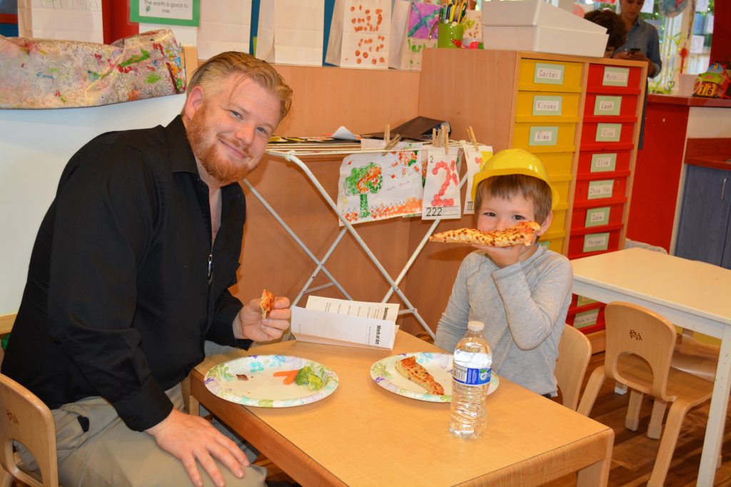 Father and son eating pizza at a table in Eyas Montessori classroom for Father's Night event
