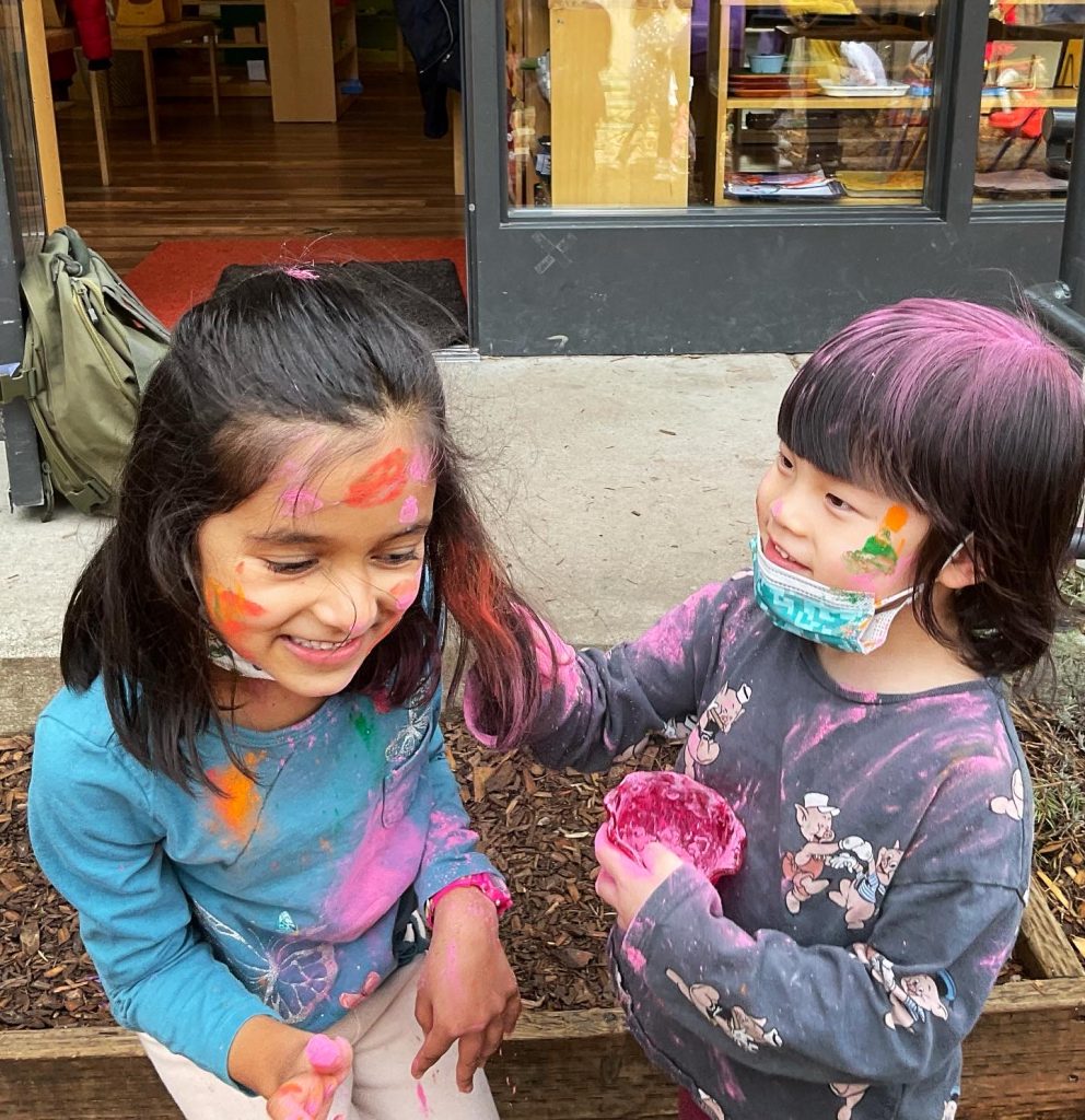 Children painting each other's hair outdoors at Eyas Montessori during Holi event