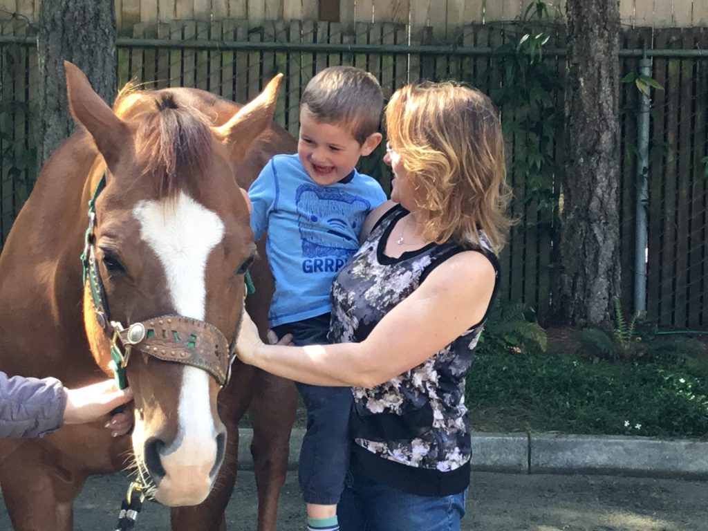 Adult holding a child petting a pony during Eyas Montessori in house field trip